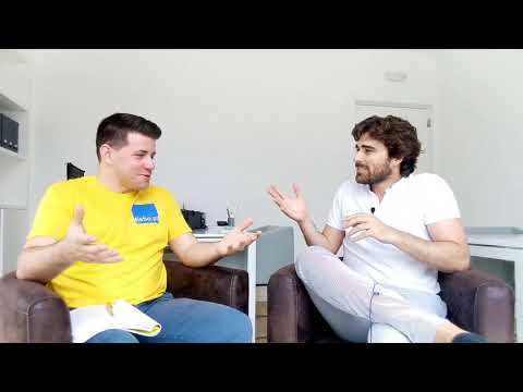 Dois homens sentados em poltronas num escritório claro, a meio de uma conversa; o entrevistador, de t-shirt amarela, segura um caderno de notas.